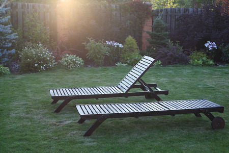 Two wooden chaise lounges in beams of the setting sun.の写真素材