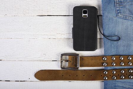 Man's concept set - Leather belt with metal rivets, smartphone and blue jeans on a wooden background.の写真素材