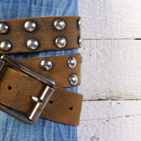 The blue jeans which are tied up by a leather brown belt with a metal buckle on old white plank background.の写真素材