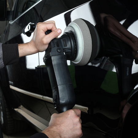 The worker polishes a car cowl with the electric tool. Close up.