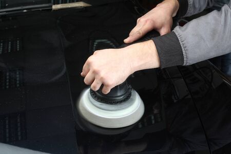 The worker polishes a car cowl with the electric tool. Close up.