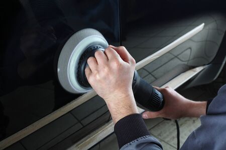 The worker polishes a car cowl with the electric tool. Close up.