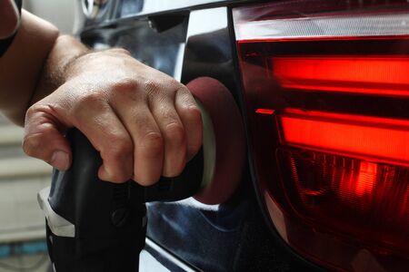 The worker polishes rear optics of headlights of the car with the electric tool. Closeup