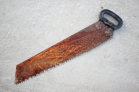 Old rusty hand saw closeup on a concrete background.の写真素材