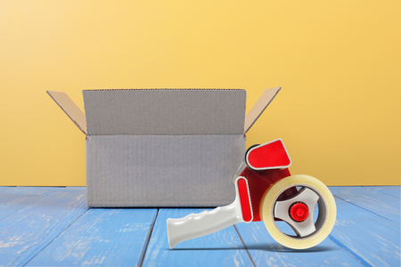 Postage and packing service - Open Package and tape dispenser front view on a blue wood and yellow wall background.の写真素材