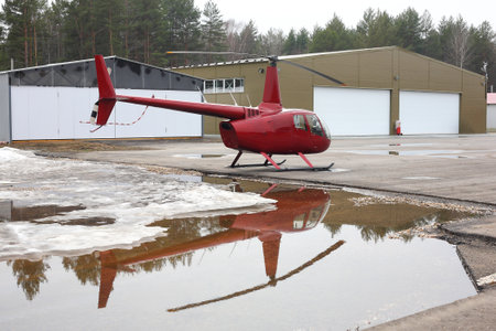Aircraft - Small red helicopter on the parking against the background of hangars.のeditorial素材
