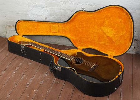 Musical instrument - brown cutaway acoustic guitar in hard case on a wood background.の写真素材