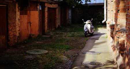 Retro transport - lonely old motor scooter among ruins of buildings in beams setting the sun
