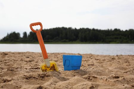 Baby shovel and bucket in sand on the river bank and wood backgroundの写真素材