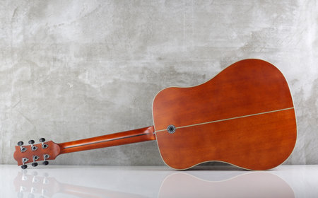 Musical instrument - Back view western acoustic guitar background of a concrete wall with a...
