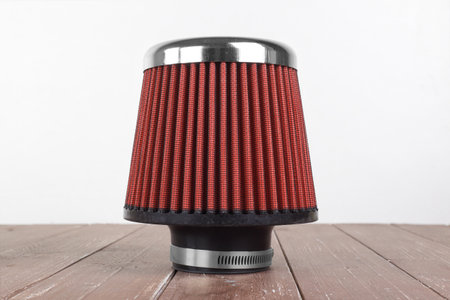 Car Parts - Side view closeup red cone sports air filter on a background of a white wall and a wooden tableの写真素材