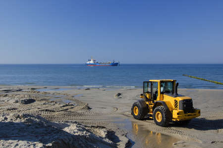 A DREDGE SHIP AND OFFSHORE CONSTRUCTION MACHINE ON THE BEACH - A ship offshore dredge pumps sand to shore. Coastal restoration project.の写真素材