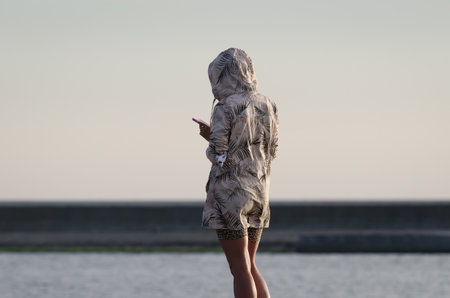 SWINOUJSCIE, WEST POMERANIAN - POLAND - 2020: A woman with a smartphone is walking on the sea beachのeditorial素材