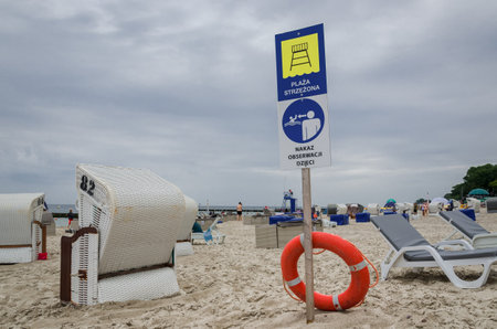 KOLOBRZEG, WEST POMERANIAN - POLAND - 2021: Information and warning sign and wicker baskets for tourists on the sea beachのeditorial素材