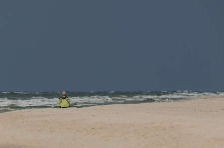 WEATHER AT THE SEASIDE - Holidaymaker walks on the beach against the background of dark stormy storm clouds over the seaの写真素材