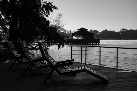 LANDSCAPE BY LAKE - Morning sun over the wooden lounge chairs in the drops of morning dew on the viewing platformの写真素材