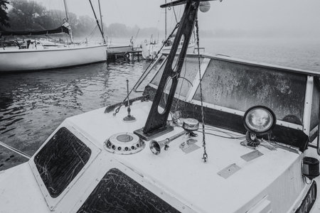 LANDSCAPE BY THE LAKE - An old motorboat and sailboats in the background on a foggy dayの写真素材