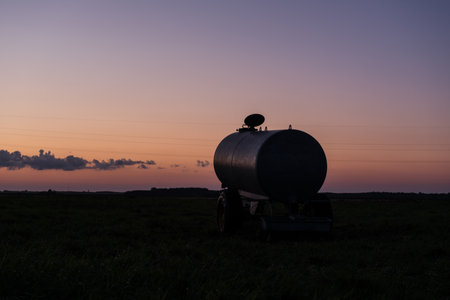 DRINKINK WATER TANK AND SUNSET - A vehicle in a pasture with a water trough for cowsの写真素材