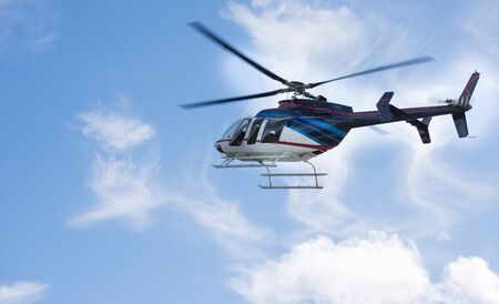 Helicopter flying through a blue sky with cloudsの写真素材