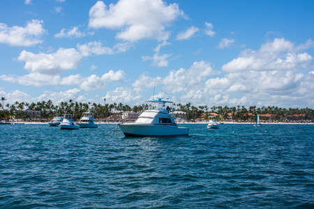 A white fishing boat stands on a dock near the shore, against a backdrop of palms and a blue sky with cloudsの写真素材