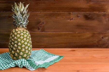 A ripe pineapple lies on a green towel on a wooden table and a wooden background.の写真素材