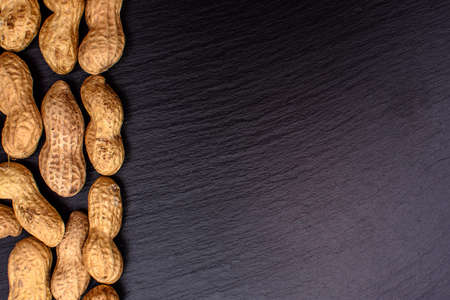 Unclean peanuts lie on a black stone board in the form of a frame, space for text.の写真素材