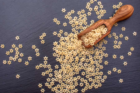 pasta in the form of asterisks lie in a wooden spoon on a black stone board, space for text.の写真素材