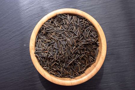 Black rice lies in a wooden plate on a black stone slate board with space for text..の写真素材