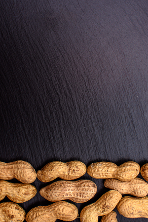 Unclean peanuts lie on a black stone board in the form of a frame, space for text.の写真素材