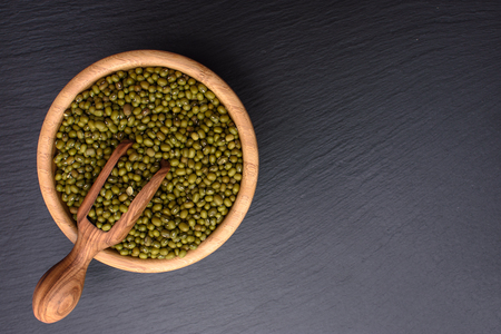 mung bean in a wooden cup and wooden scoop on a black stone board background, space for text, beans.の写真素材