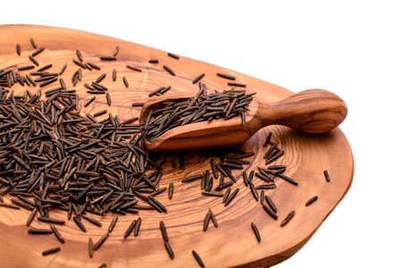 Black rice on an olive board with a wooden scoop isolated on a white background.の写真素材