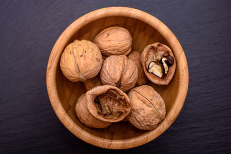 Walnuts in a wooden cup on a black stone board background, frame space for text.