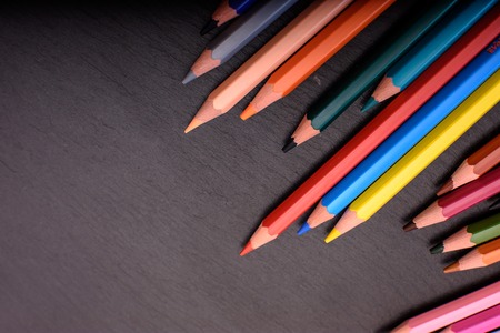 Many colored pencils on a black stone slate, place for text.の写真素材