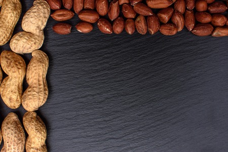 Untreated peanuts and peeled on a black stone board, space for text.