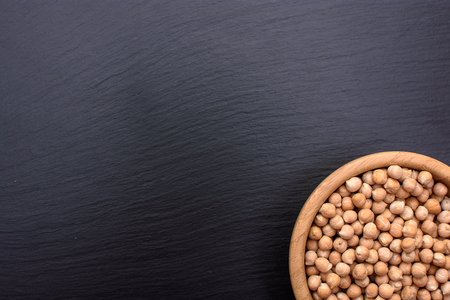Peeled chickpeas lies in a wooden cup on a stony black board, black background, space for text.の写真素材