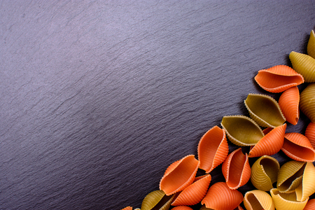 Colored pasta lie on black stone board from slate background, place for text.の写真素材