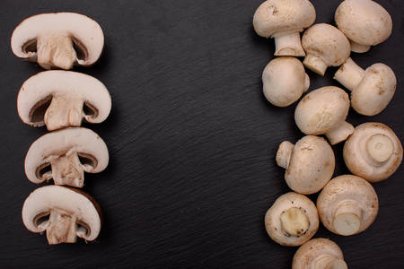 White mushrooms champignons whole and sliced lie on a stone black slate board, background.の写真素材