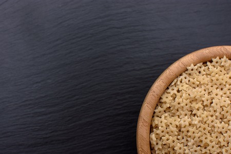 Macaroni in the form of asterisks lie in a wooden cup on a black stone board, space for text.の写真素材