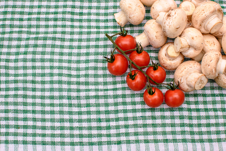 White mushrooms champignons and red cherry tomatoes lie on a green towel, place for textの写真素材