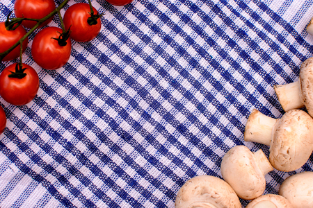 White mushrooms champignon and red cherry tomatoes lie on a blue towel, space for text, background.の写真素材