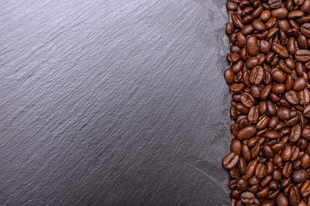 Stony black board sprinkled with nearby grain roasted coffee, place for tex, background and texture.