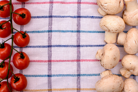 Gray mushrooms champignons and red cherry tomatoes lie on a plaid towel, place for text.の写真素材