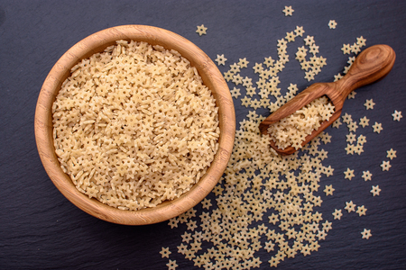 pasta in the form of starlets lie in a wooden cup and a wooden scoop on a black stone board, space for text.の写真素材
