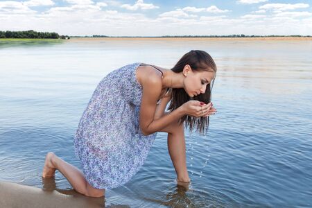 Young woman drinking clean water from Lakeの写真素材