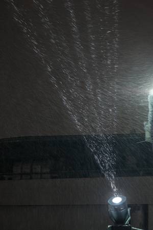 Searchlight ray shines on flying snowflakes at nightの写真素材