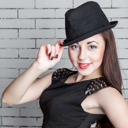 Portrait of stylish young woman in a hat against a brick wall