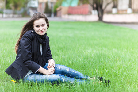 Beautiful young woman sits on a green lawn in the cityの写真素材