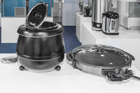 Electrical kitchen equipment, electric pressure cooker and frying pan in the foreground