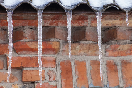 Icicles on the roof of the house in front of brick wall, winter backgroundの写真素材