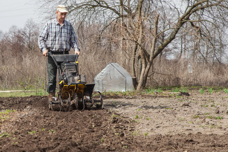 Man working in the garden with garden tiller. Garden tiller to work. Man with tractor cultivating...